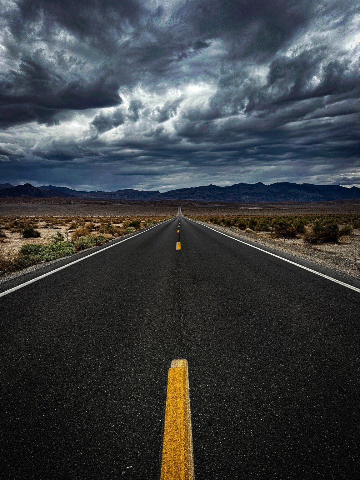 Desert highway stretching toward mountains beneath storm clouds.